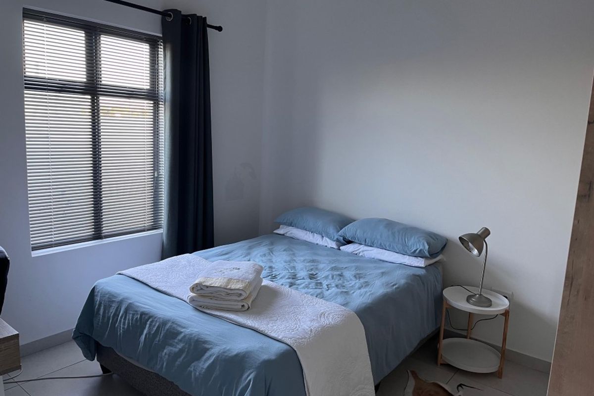 A functional bedroom featuring tiled flooring, a large window with fitted blinds, and neutral wall finishes.