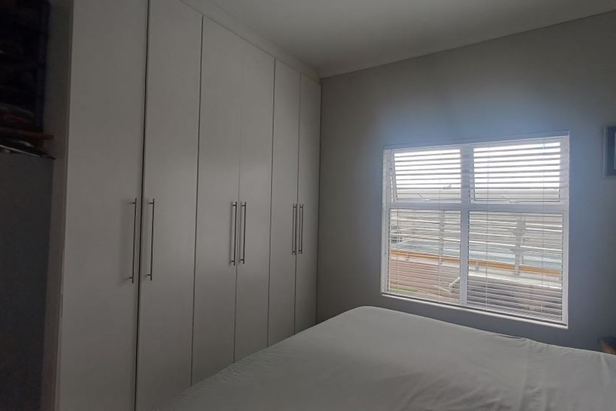 A well-maintained bedroom featuring built-in floor-to-ceiling wardrobes and a window with fitted horizontal blinds.