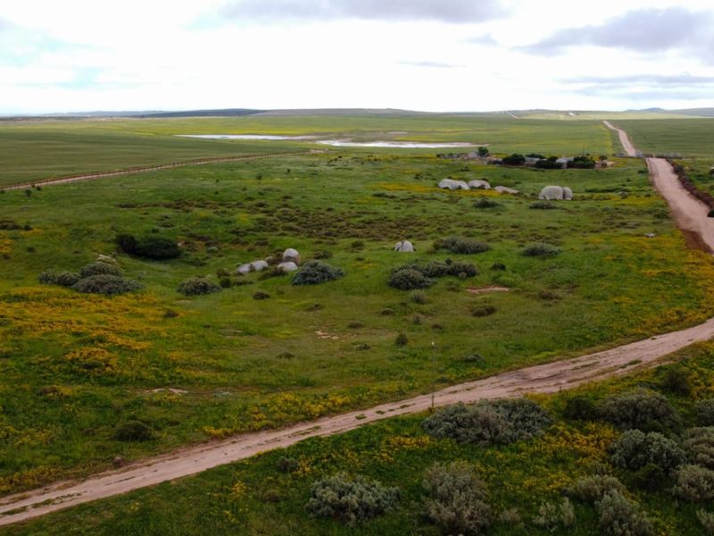 An aerial view of a large, undeveloped residential land parcel featuring natural vegetation, a dirt access road, and perimeter fencing.