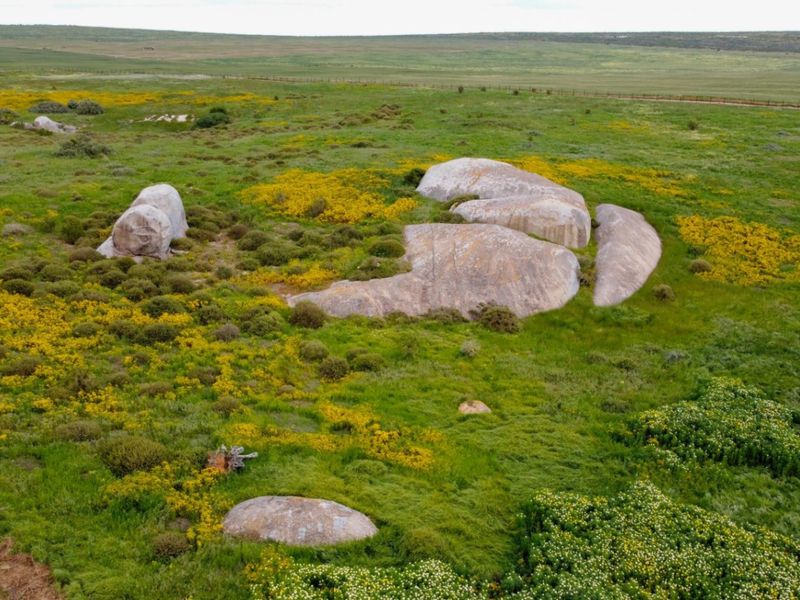 An aerial view of a vacant residential plot featuring natural rock formations and native grassland vegetation.