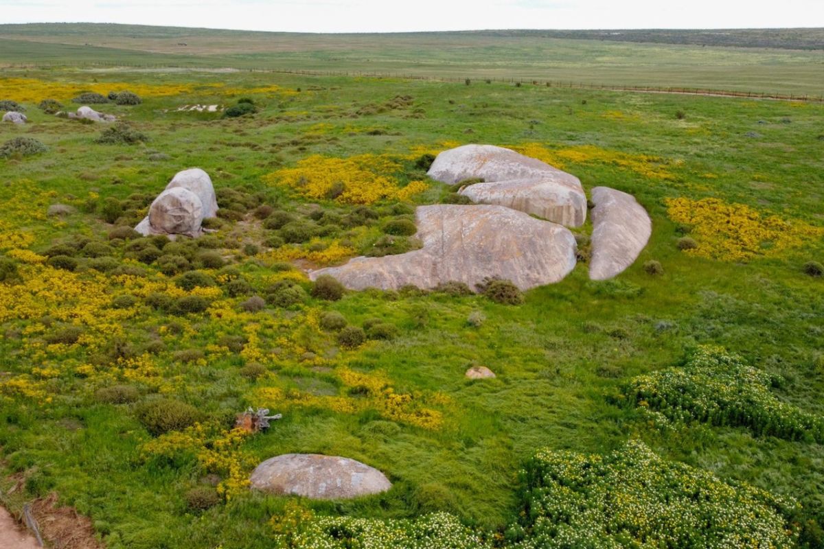An aerial view of a vacant residential plot featuring natural rock formations and native grassland vegetation.