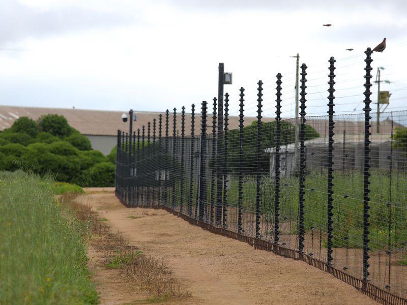 A view of the property boundary featuring secure electric fencing and integrated security surveillance cameras along a dirt access path.