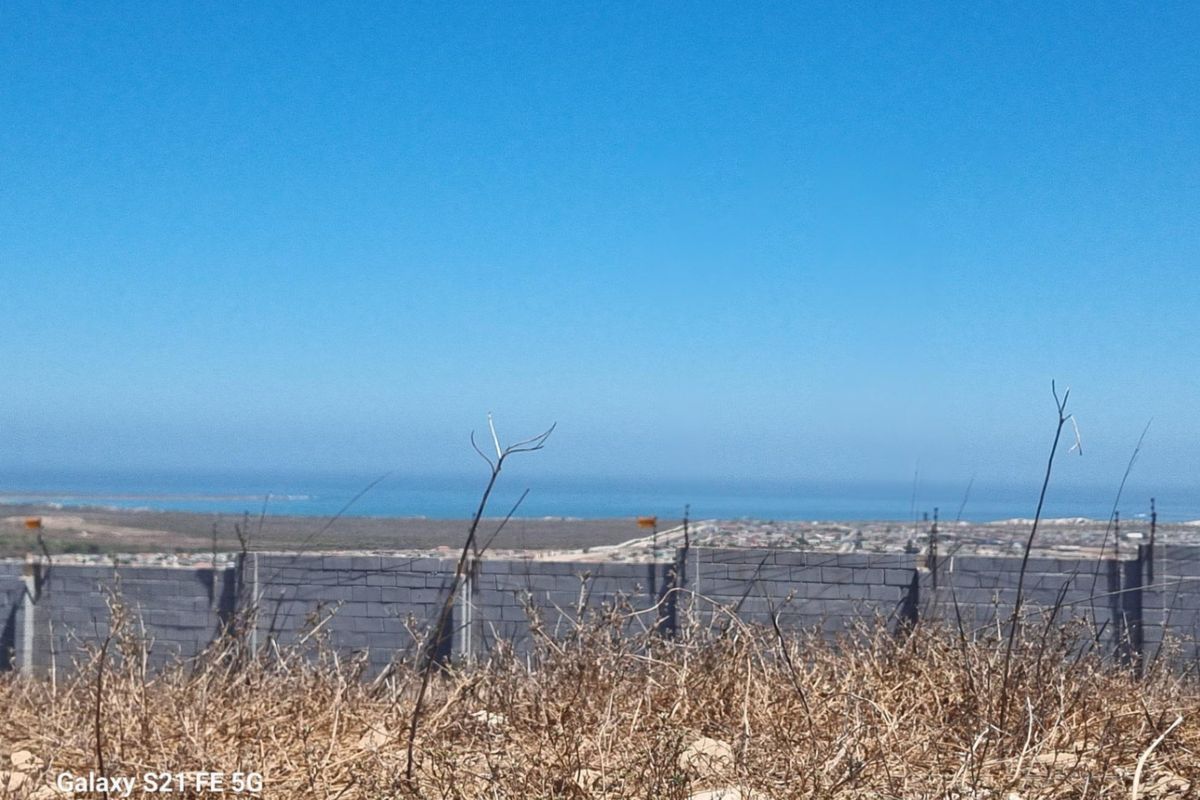 A view of the surrounding landscape and distant coastline from the vacant residential plot, featuring a perimeter wall with electric fencing.