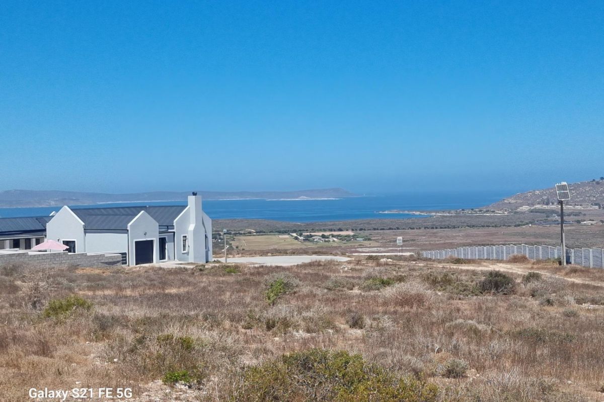 A scenic view of the coastal landscape and ocean from the vacant residential land, featuring nearby property and perimeter fencing.