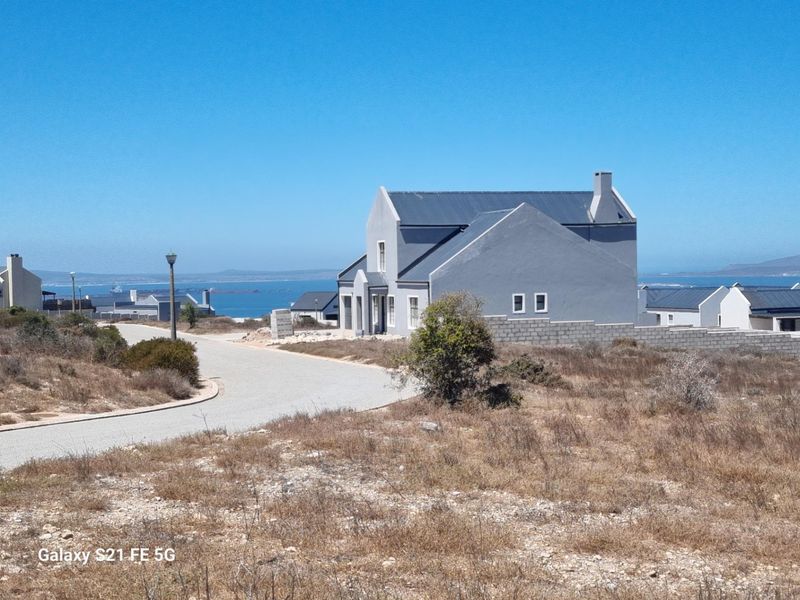 A view of a modern grey residential property situated in a coastal estate with paved road access and distant ocean views.