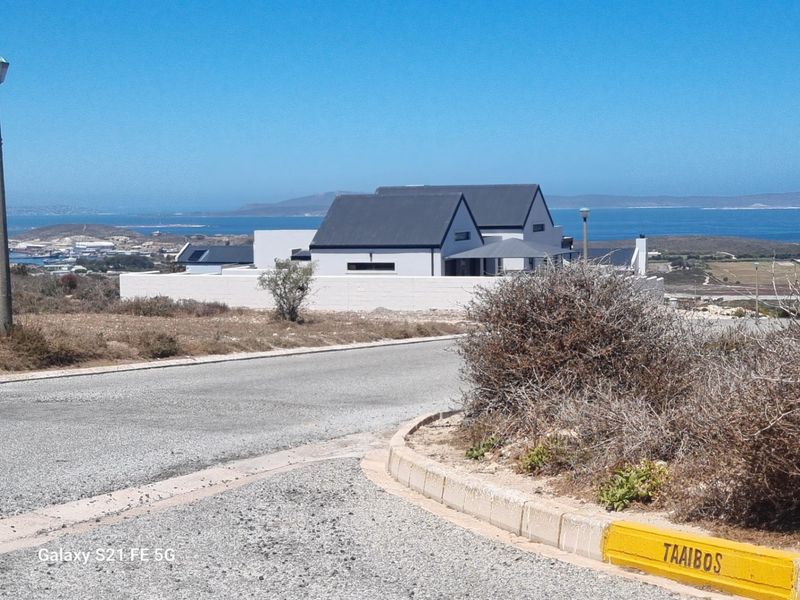 A street-level view of a modern residential property featuring a white boundary wall, with a scenic coastal landscape in the background.