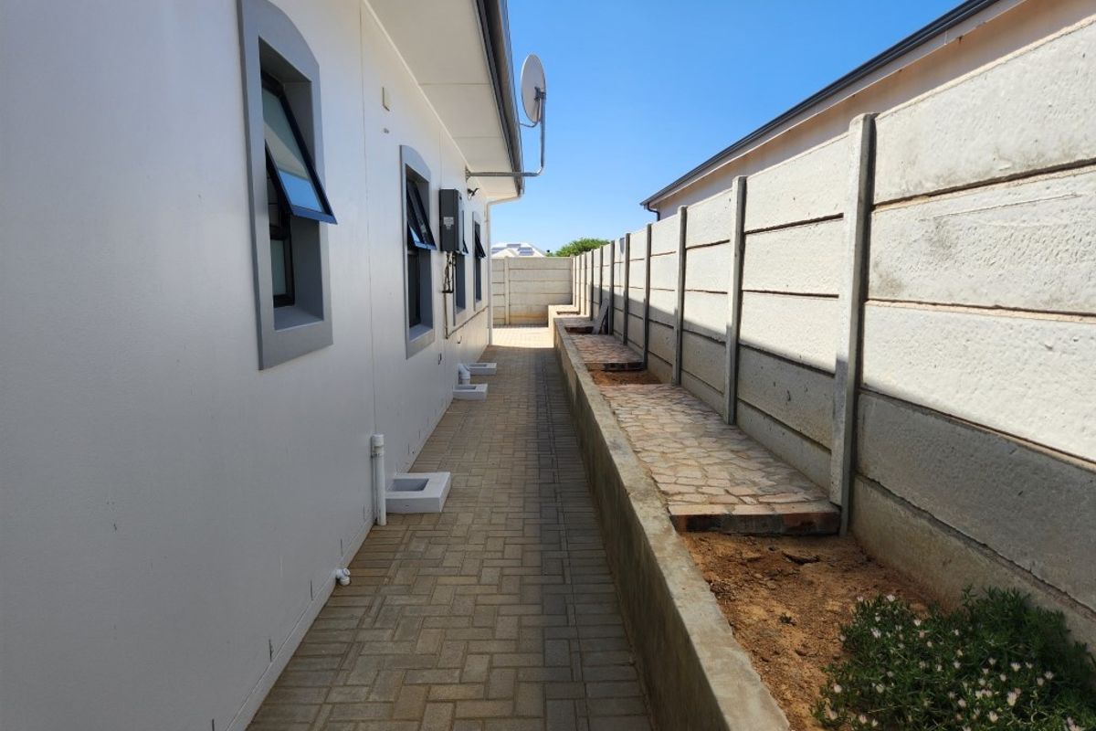 A side exterior walkway featuring paved flooring, a concrete boundary wall, and external wall-mounted drainage pipes.