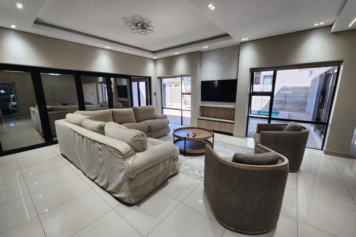 Spacious modern living room featuring large format floor tiles, recessed ceiling lighting, and expansive glass sliding doors opening to the outdoor pool area.