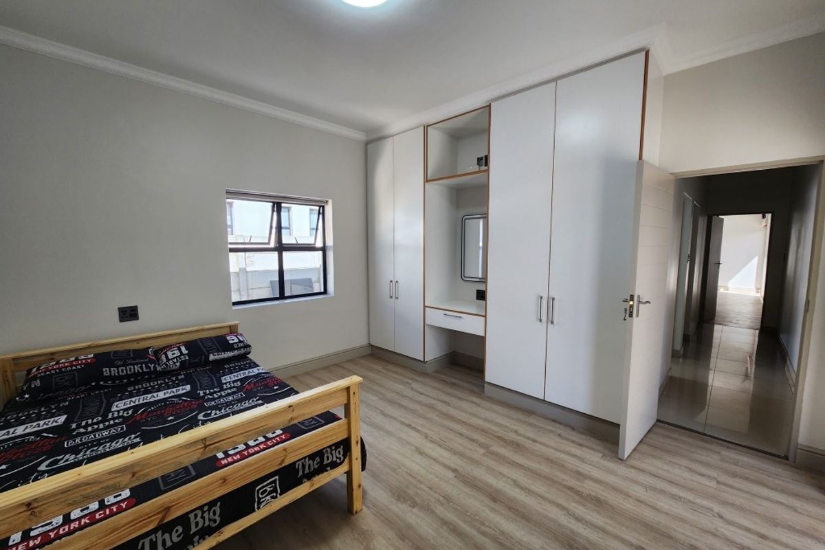 A well-maintained bedroom featuring built-in white cabinetry with an integrated vanity, light wood-look flooring, and a window providing natural light.