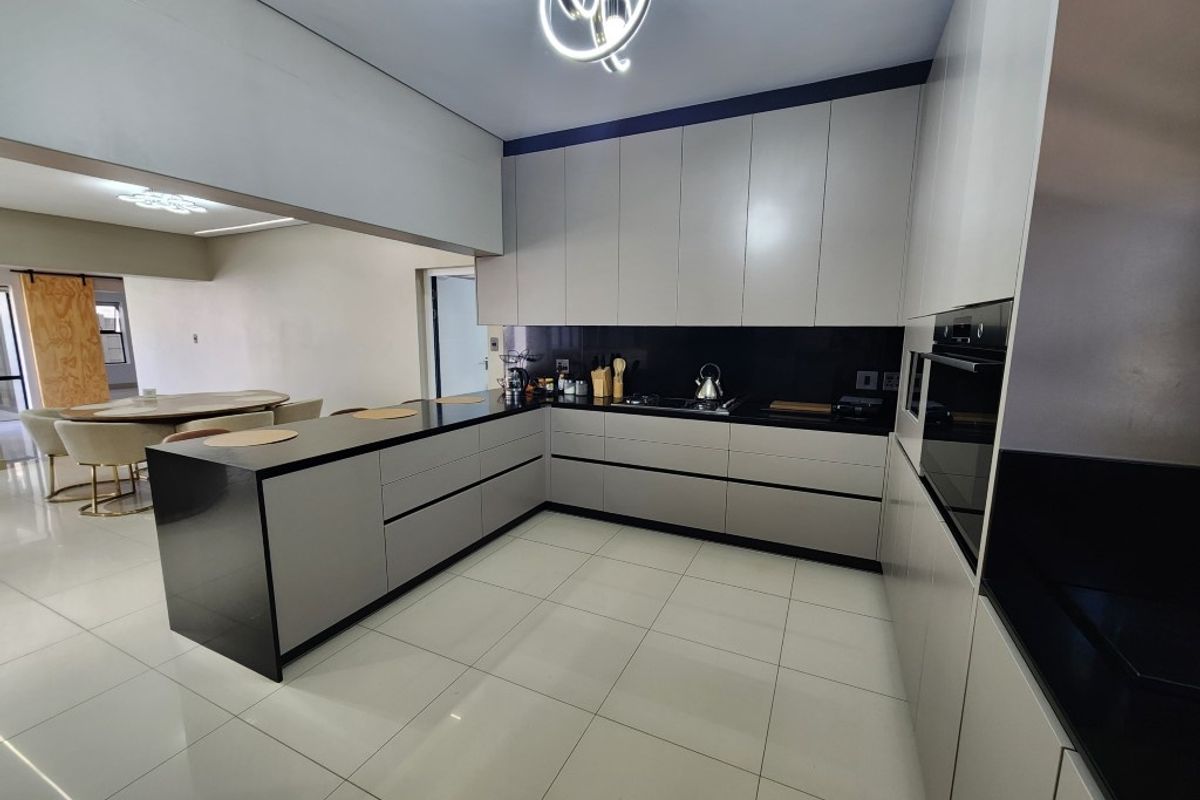 Modern open-plan kitchen featuring sleek handleless cabinetry, dark stone countertops, integrated oven, and large format floor tiles, seamlessly connecting to the dining area.