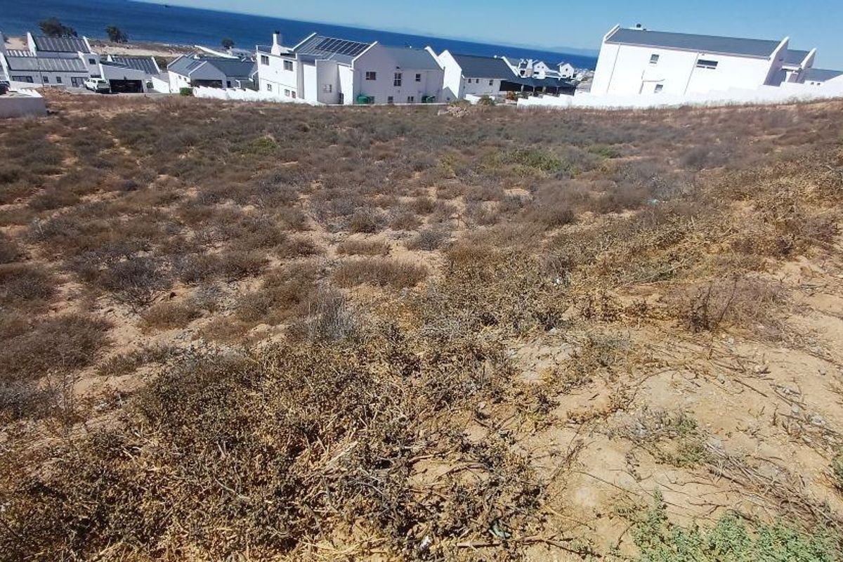 A vacant residential plot featuring natural coastal vegetation and a gentle slope, offering potential for development with views of the surrounding neighborhood and ocean.