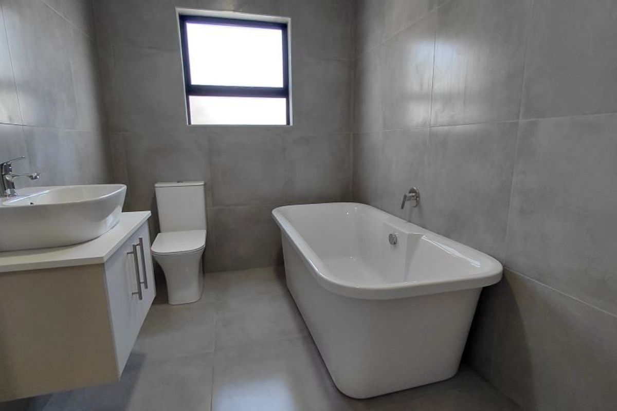 Modern bathroom featuring a freestanding bathtub, a contemporary vanity with a vessel sink, and a back-to-wall toilet, finished with large-format grey wall tiles.