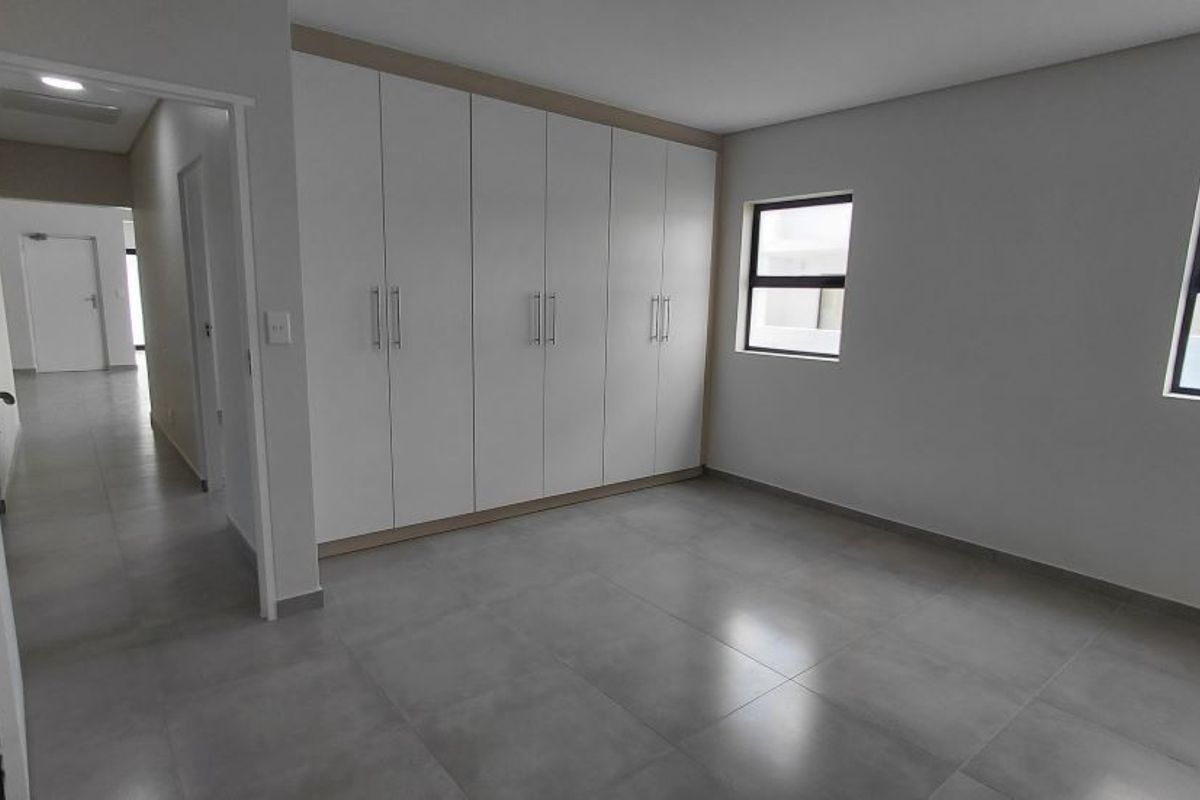 A bright, modern bedroom featuring large-format floor tiles, neutral walls, and extensive built-in floor-to-ceiling cabinetry with clean lines.