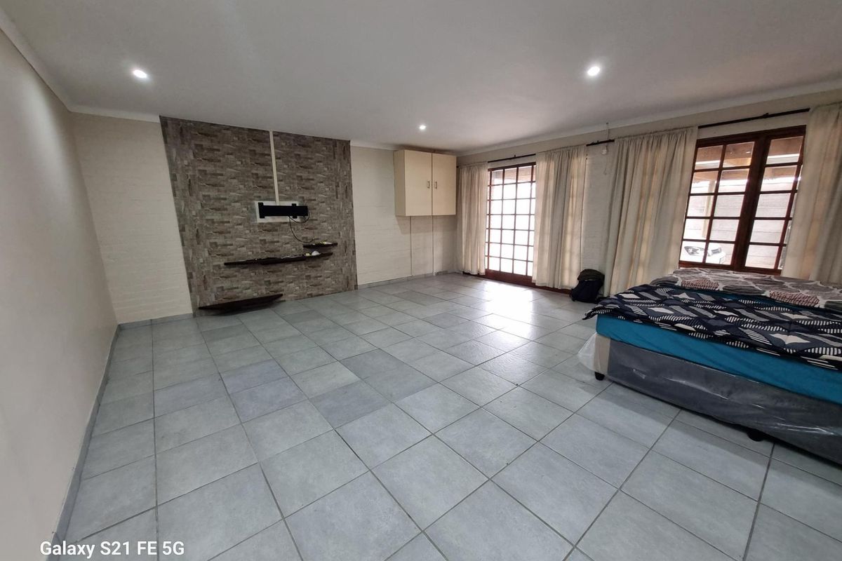 Spacious bedroom featuring large format floor tiles, a stone-cladding feature wall with built-in shelving, and direct access to the exterior through wooden framed glass doors.