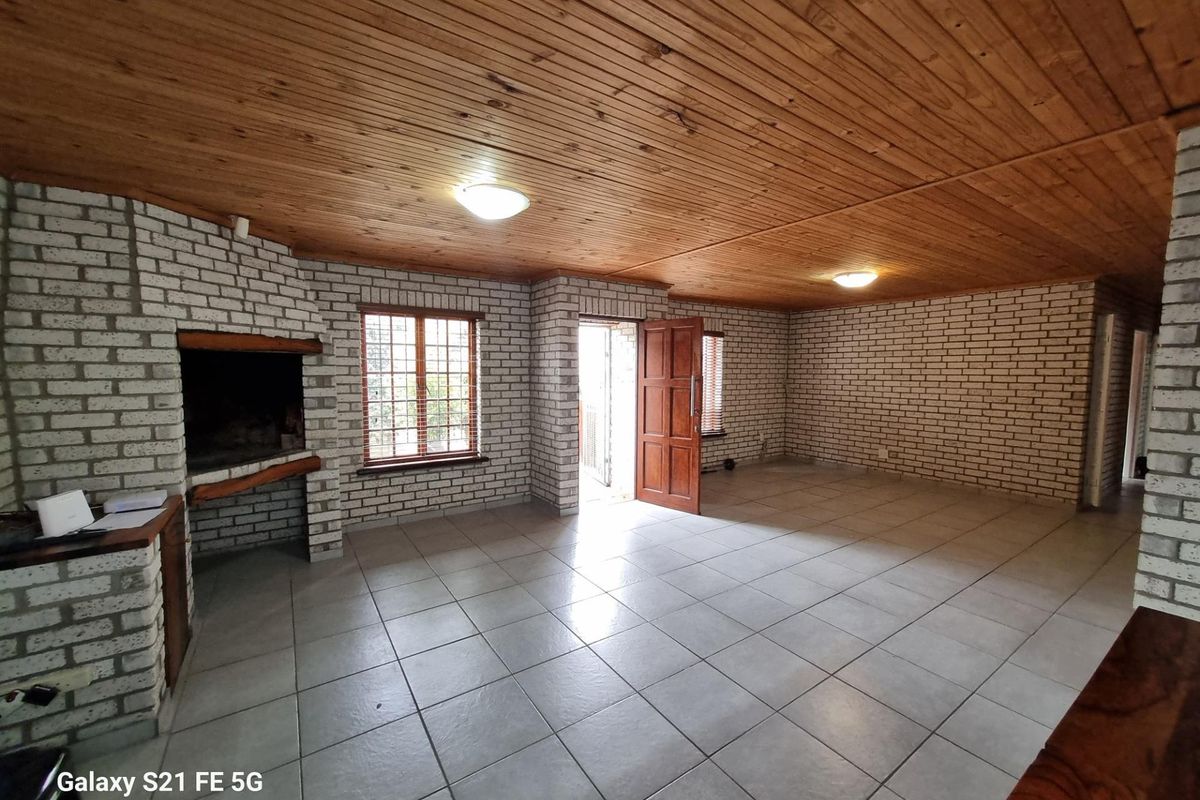 Spacious living area featuring exposed white brick walls, a built-in fireplace, tiled flooring, and a timber-clad ceiling with access to the exterior.