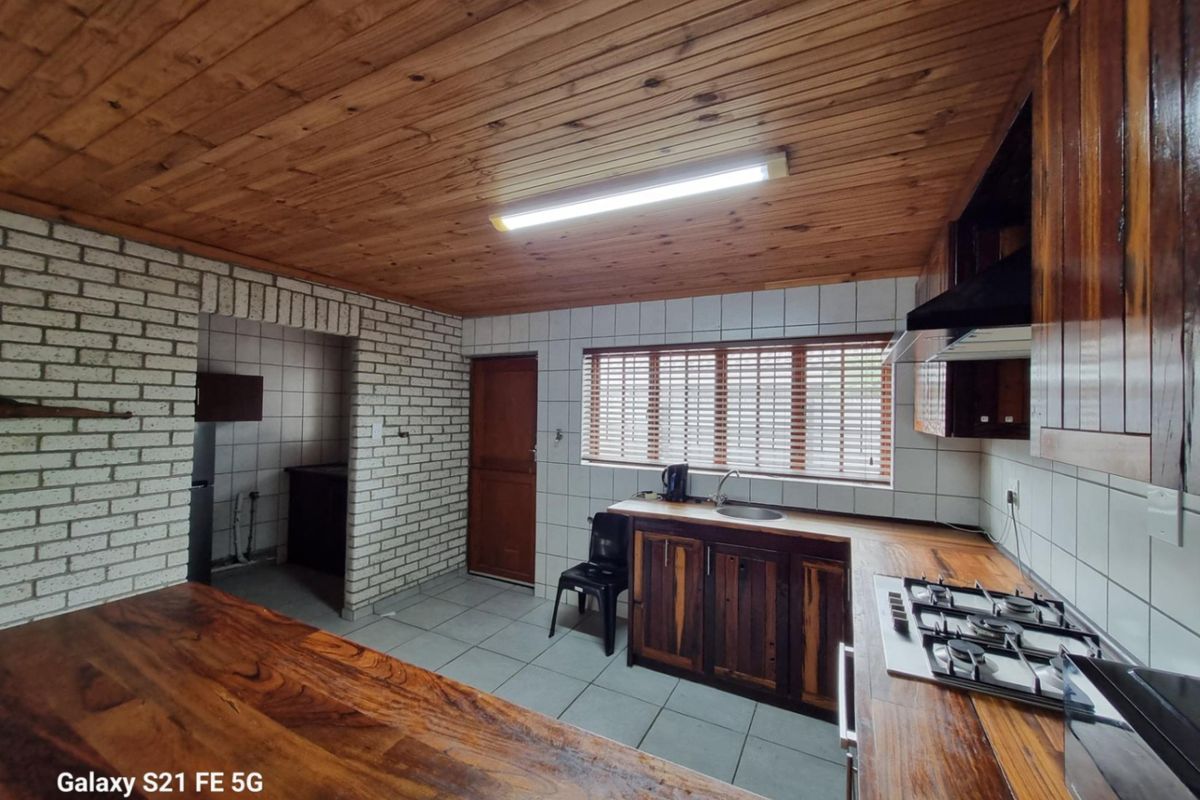 A rustic kitchen featuring wooden cabinetry, a timber-clad ceiling, a built-in gas hob, and an adjacent scullery area with brick feature walls.