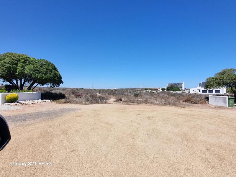 A view of a vacant residential plot featuring natural coastal vegetation, a gravel surface, and established trees, offering potential for development.