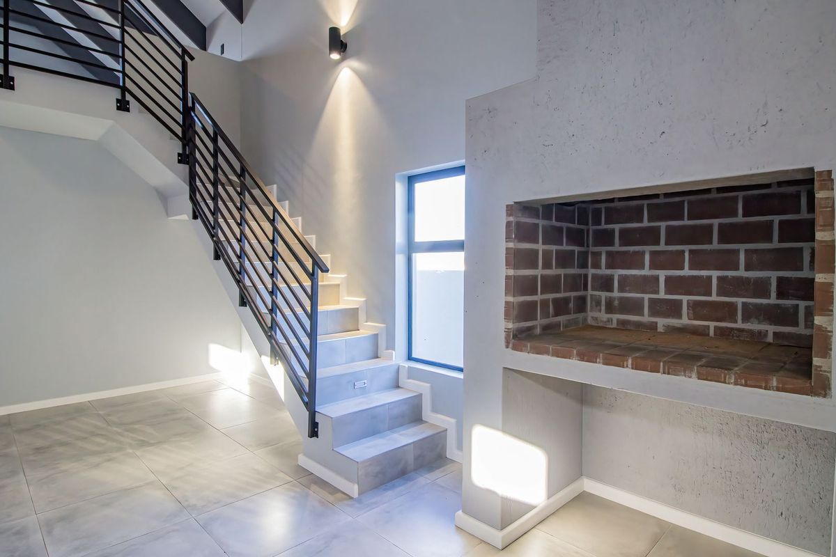 Modern living area featuring a built-in brick fireplace, tiled flooring, and a contemporary staircase with metal railings leading to the upper level.