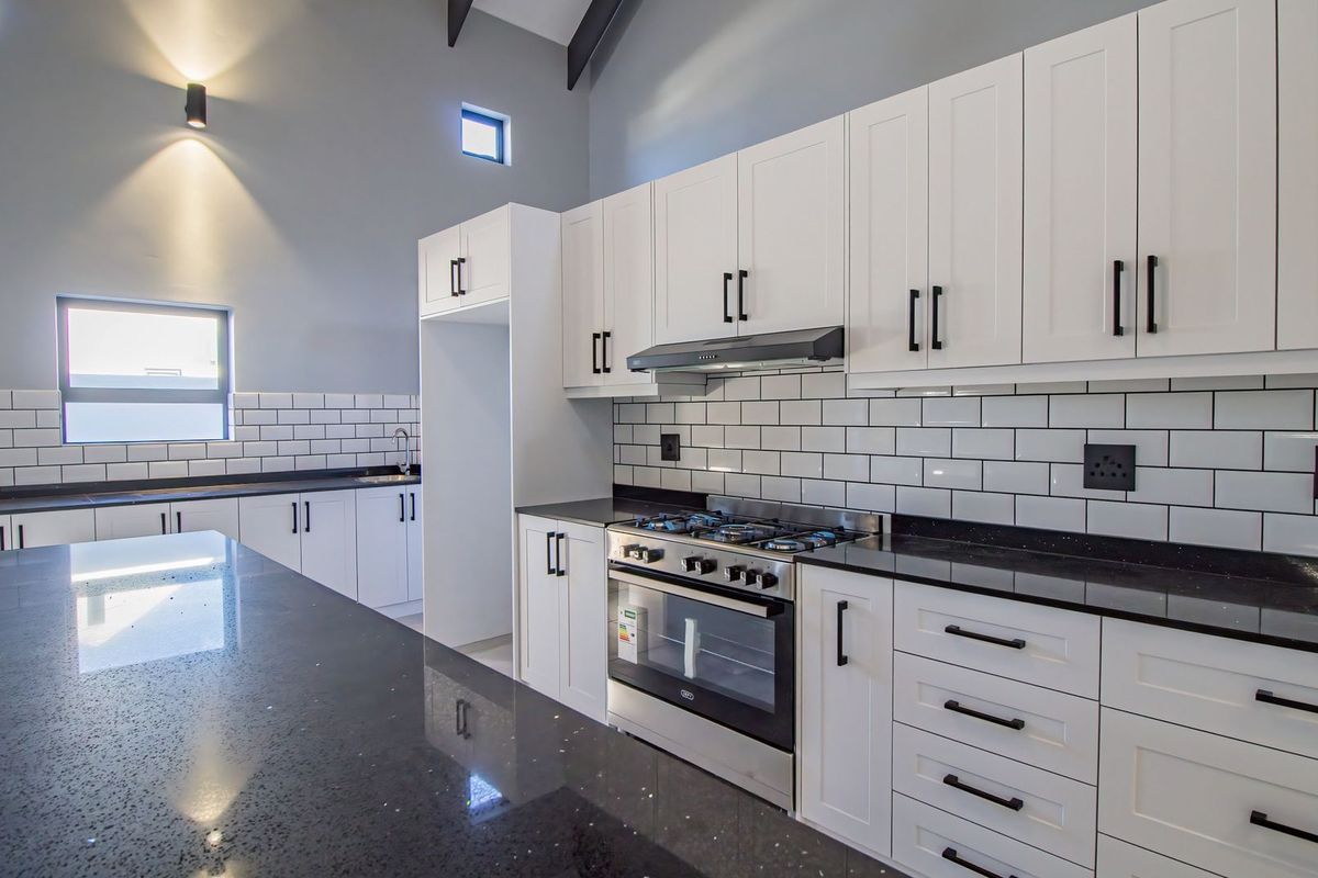 Modern kitchen featuring white shaker-style cabinetry, black granite countertops, subway tile backsplash, and a built-in gas stove with extractor fan.