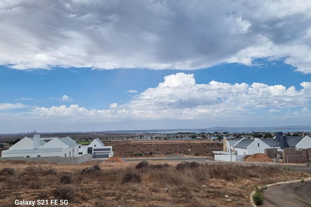 A wide-angle view of a vacant residential plot overlooking a coastal landscape and neighboring modern homes under a cloudy sky.