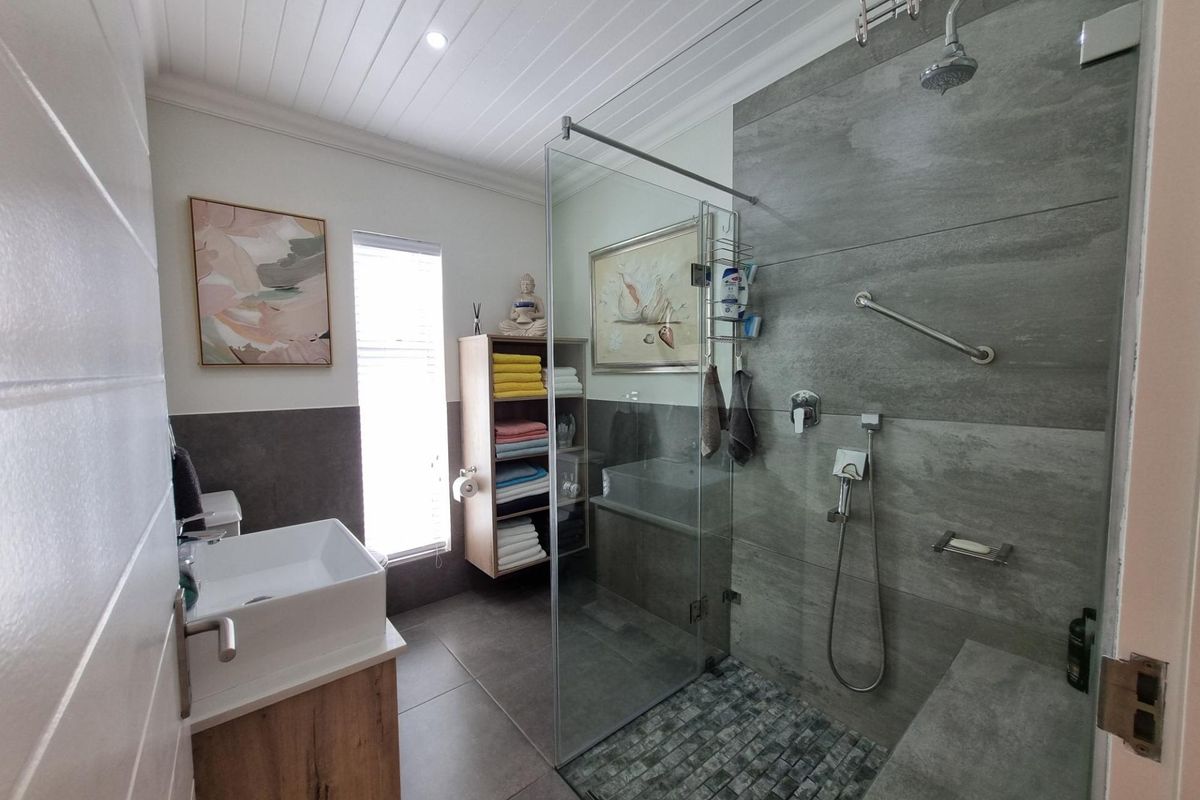 Modern bathroom featuring a walk-in shower with glass screen, stone-look wall tiles, a vessel sink vanity, and a tongue-and-groove ceiling.