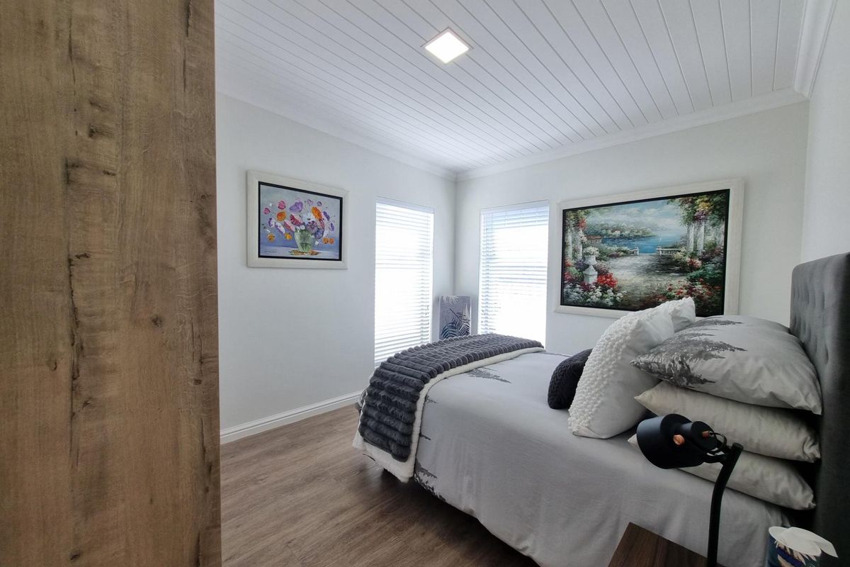 A well-maintained bedroom featuring wood-look flooring, a modern tongue-and-groove ceiling, and dual windows with fitted blinds.