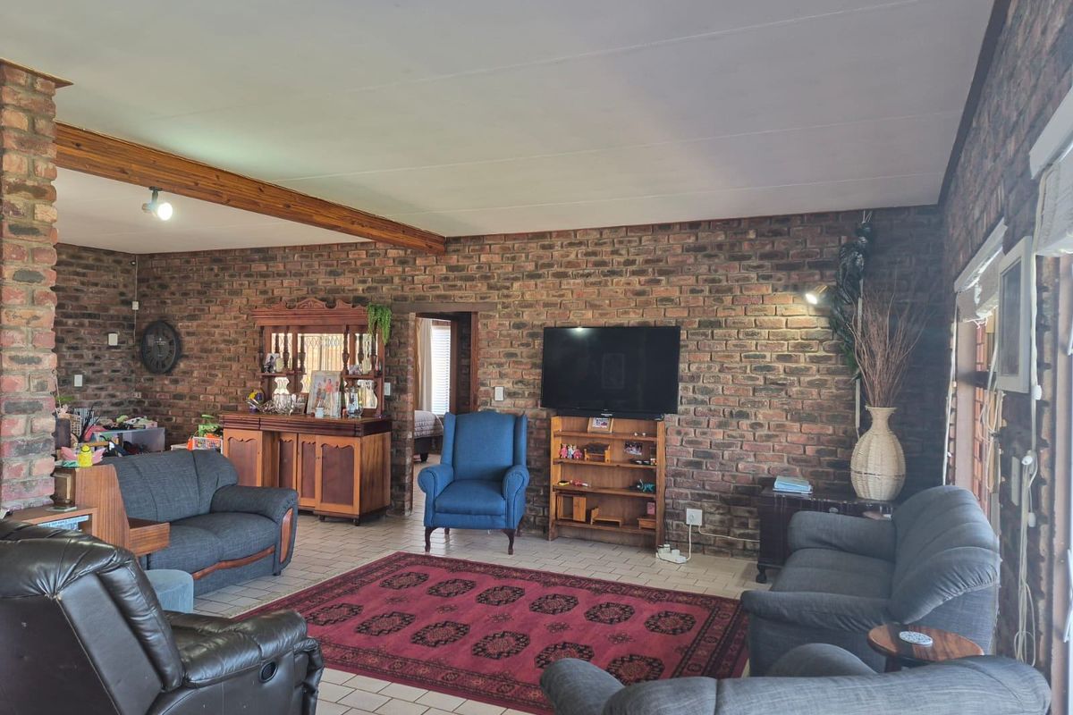 Spacious living room featuring exposed face-brick walls, tiled flooring, and a prominent timber ceiling beam, creating a rustic and character-filled atmosphere.