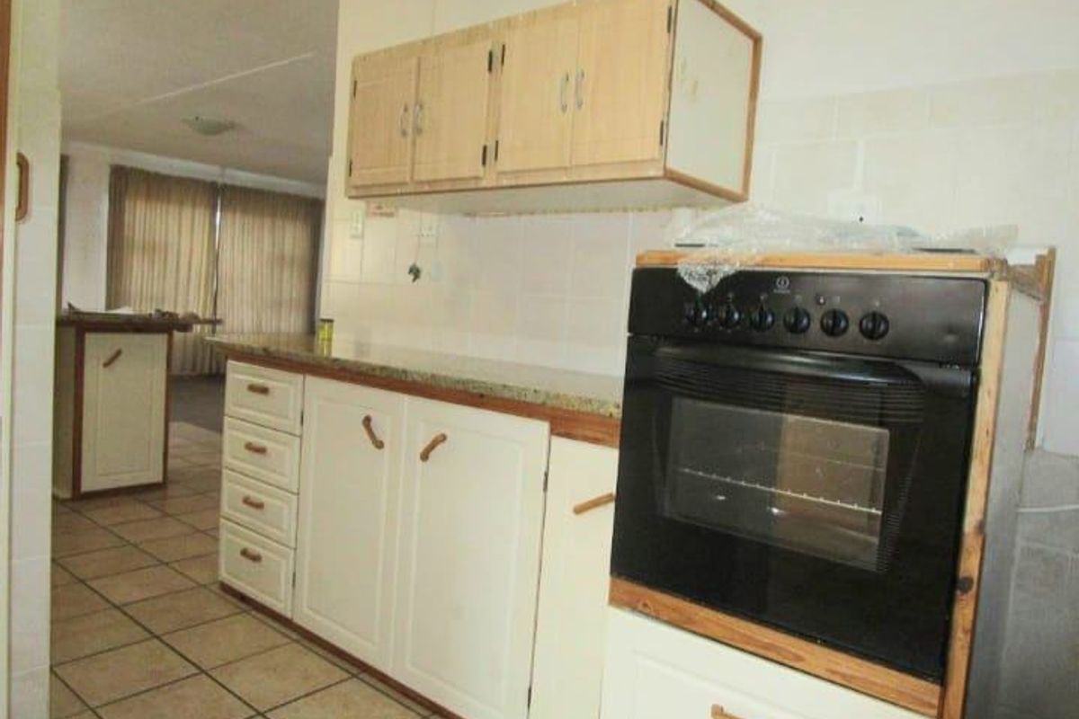 A functional kitchen featuring built-in cabinetry, tiled flooring, and a fitted oven, with an open-plan layout leading into the adjacent living area.