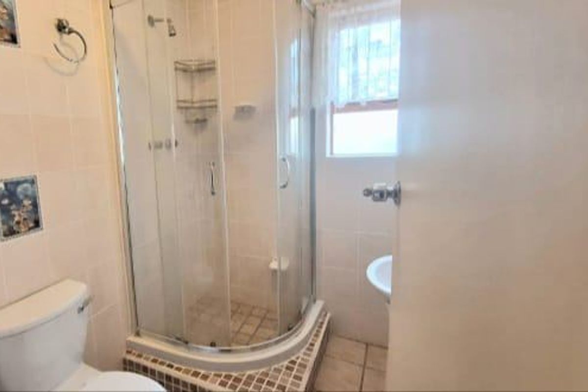 A compact bathroom featuring a corner shower enclosure, pedestal basin, and standard toilet with neutral wall tiling.