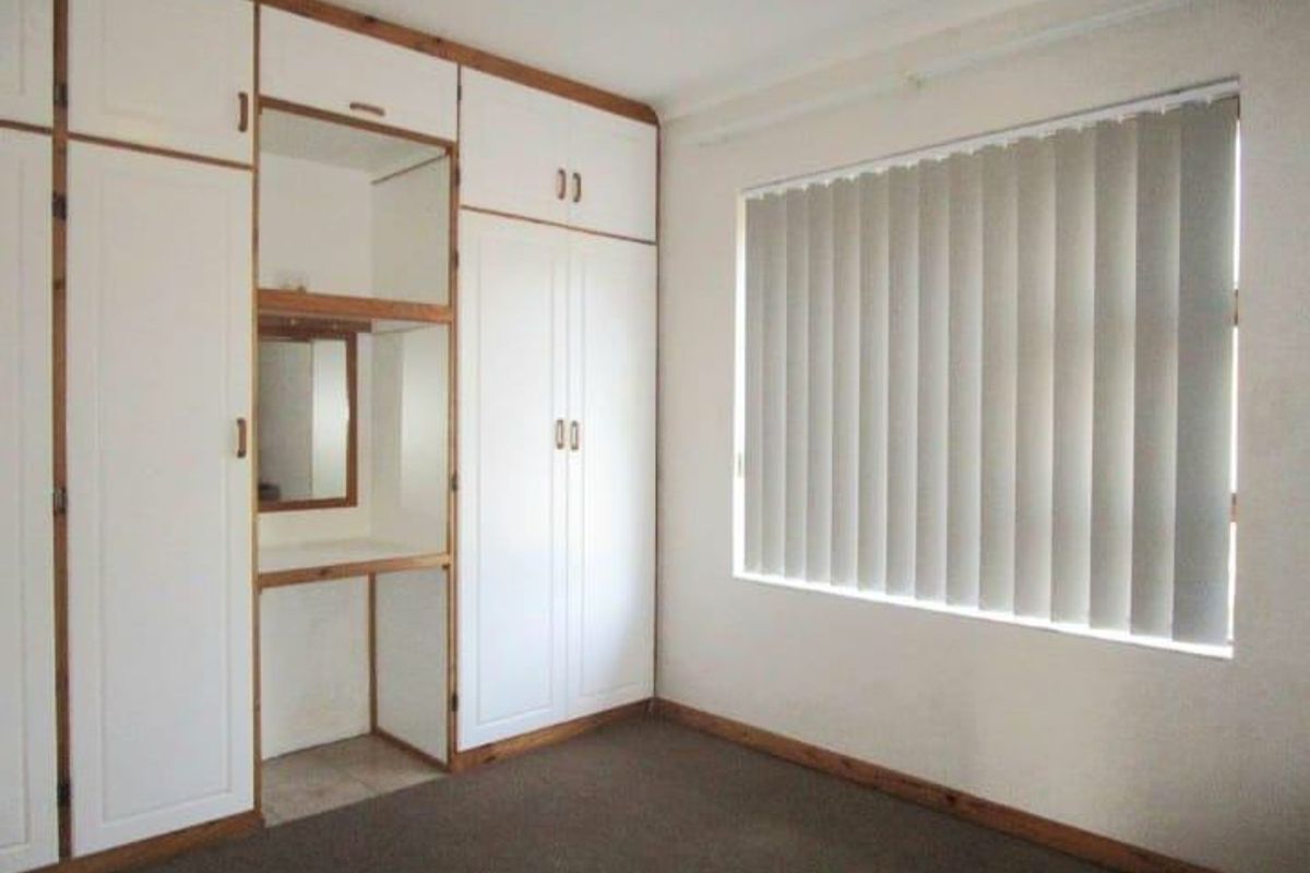 A bedroom featuring extensive built-in white cabinetry with integrated vanity and vertical window blinds.