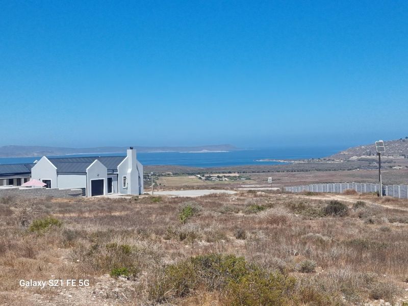 A scenic view of the coastal landscape and ocean from the vacant residential land, featuring nearby property and perimeter fencing.