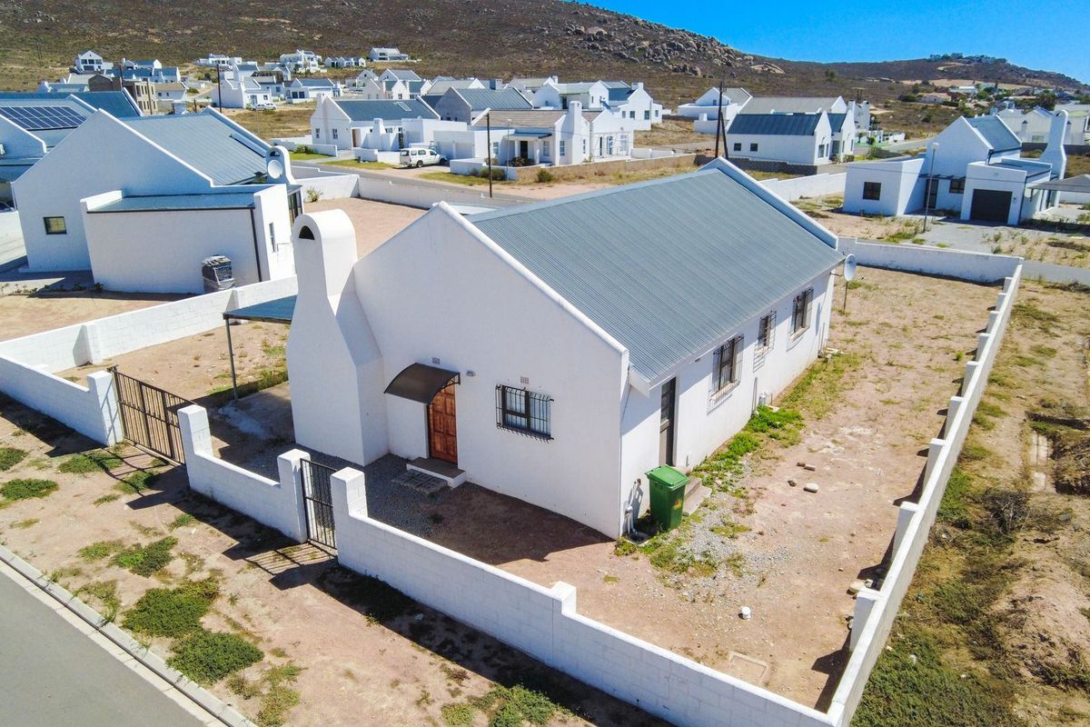 Aerial view of a detached house featuring a white facade, metal roof, external chimney, and a walled perimeter in a coastal residential estate.