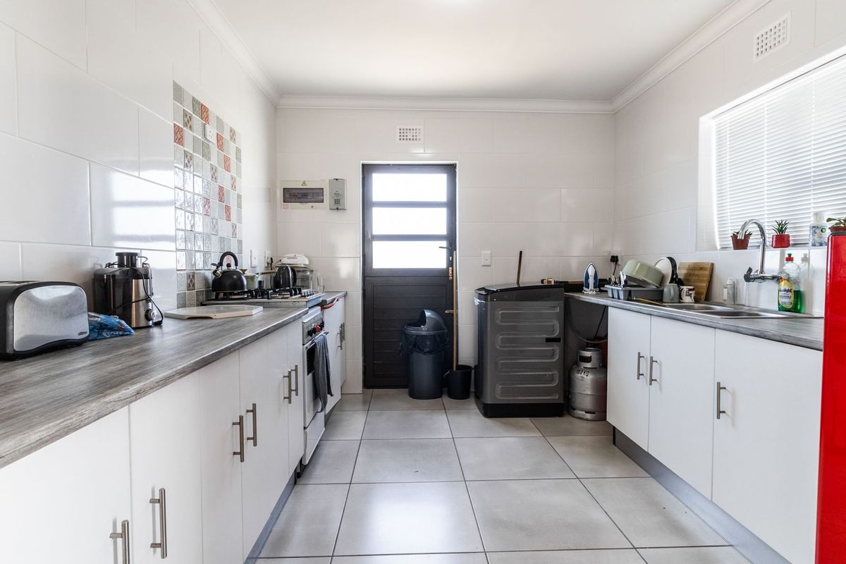 A functional kitchen featuring white cabinetry, tiled walls, a gas stove, and a stainless steel sink, with direct access to the exterior.