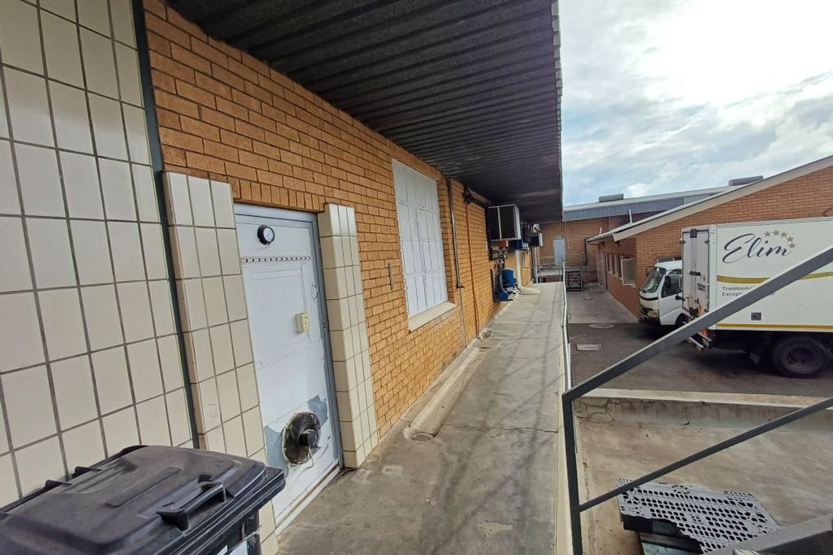 Exterior side walkway of an industrial property featuring brick facade, metal roofing, and access door with integrated ventilation.