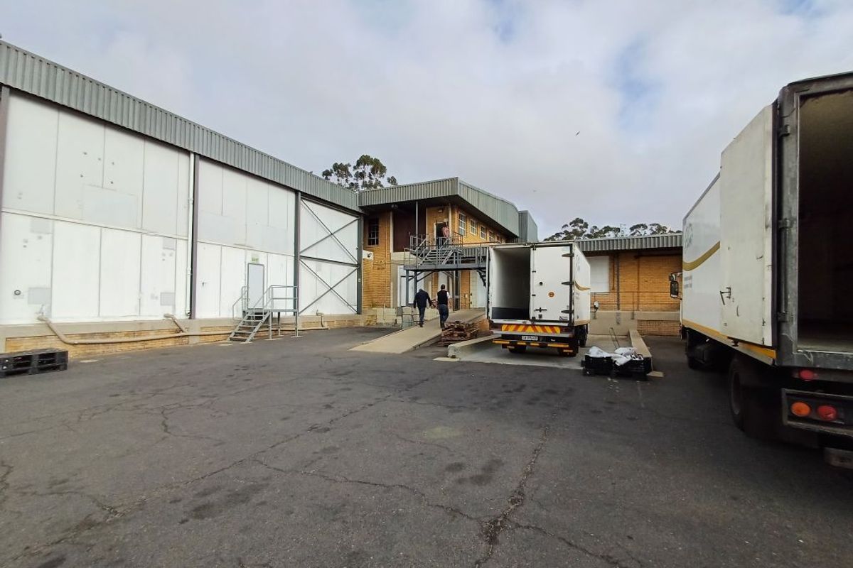 Industrial loading bay area featuring a concrete ramp, metal staircase, and large warehouse facade with asphalt yard space for logistics and transport access.