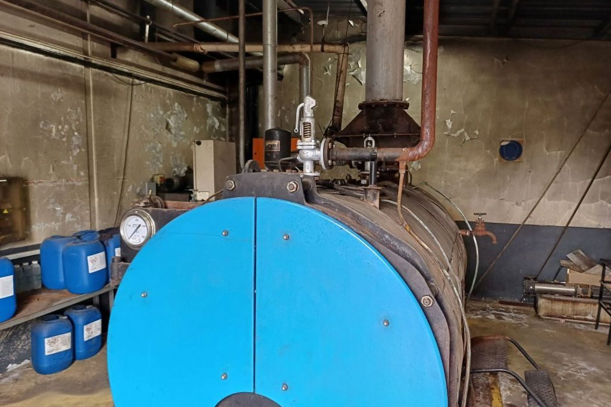 Industrial utility space featuring a large boiler unit with exposed piping and infrastructure in a functional, aged condition.