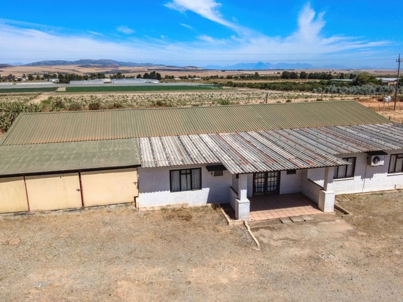 Aerial view of a farm dwelling featuring a corrugated metal roof, covered patio, and attached garage structure set within a rural landscape.