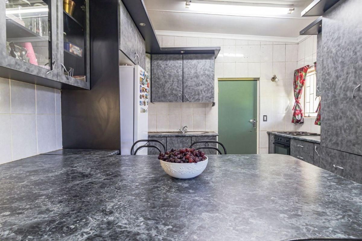 A functional kitchen featuring dark marble-effect laminate countertops, ample built-in cabinetry, a tiled backsplash, and integrated cooking appliances.