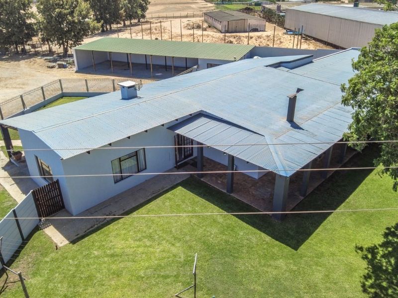 Aerial view of a farm property featuring a main residence with a corrugated metal roof, covered patio, and an adjacent outbuilding on a large lawn.