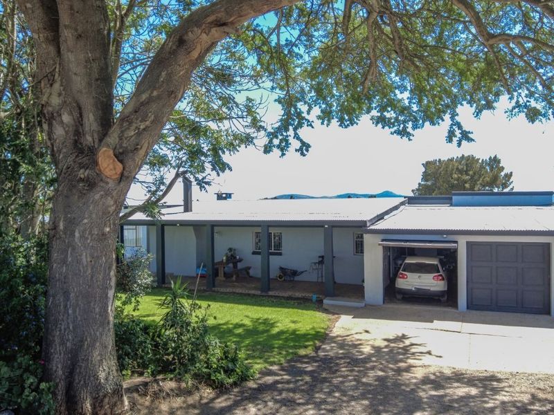 Front view of a farm-style residence featuring a covered patio, corrugated metal roof, and an integrated double garage with a concrete driveway.