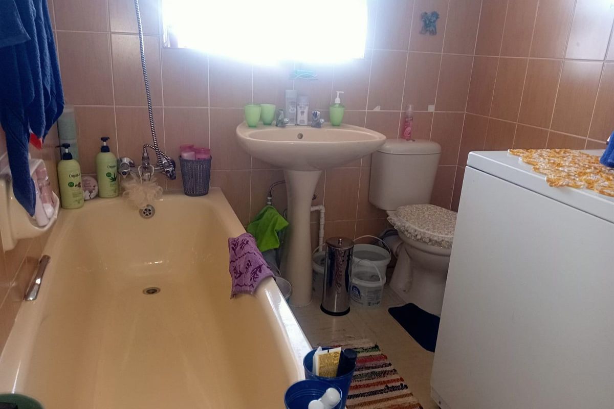 A functional bathroom featuring a pedestal basin, bathtub, and toilet with dated wall tiling, offering potential for a modern renovation.