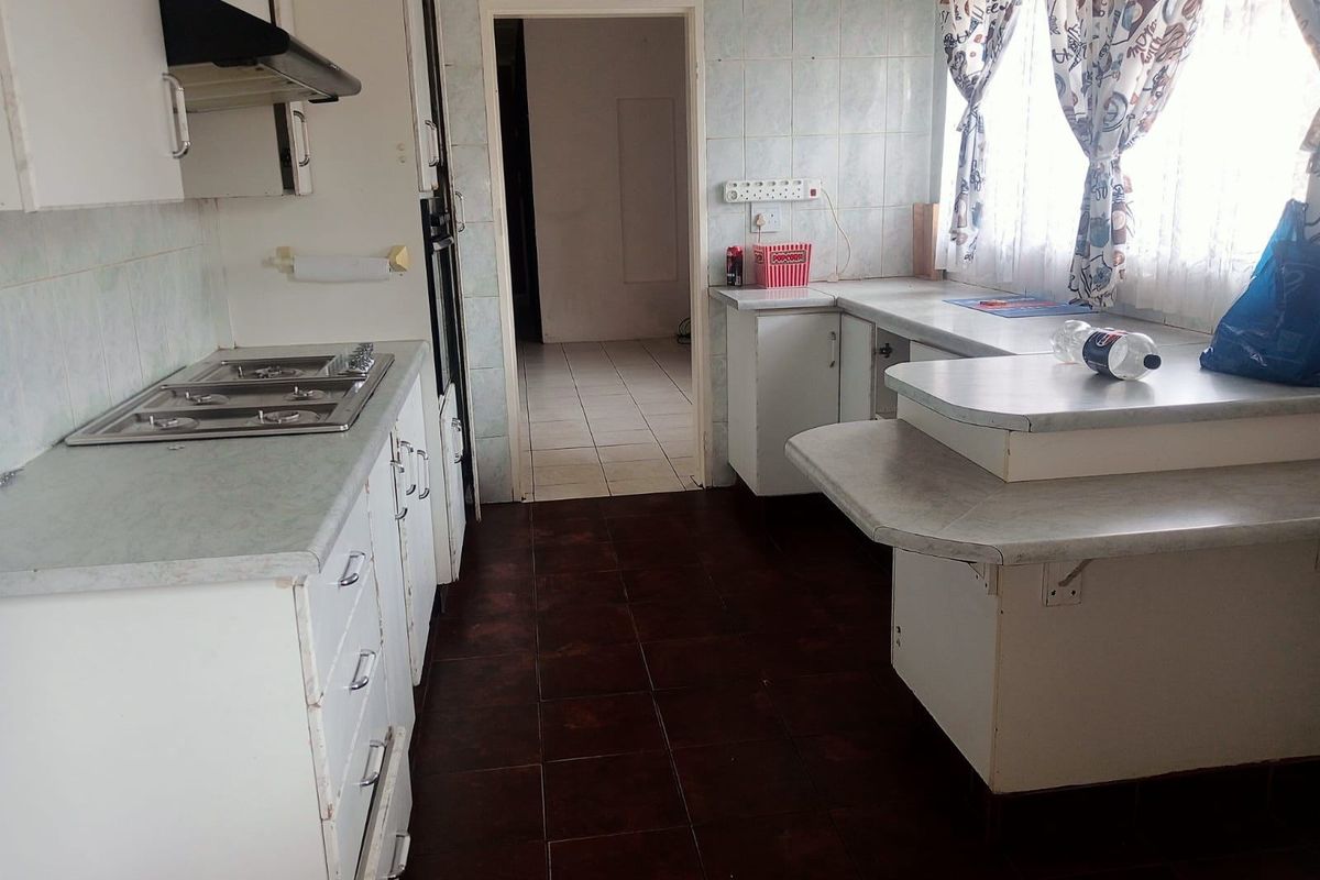 A dated kitchen featuring white cabinetry, a built-in gas hob, extractor fan, and tiled flooring, offering a functional layout with potential for modernization.