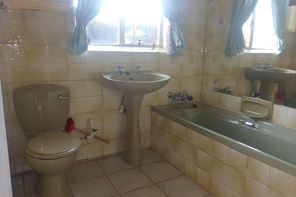 A dated bathroom featuring a pedestal sink, bathtub, and toilet with original ceramic wall tiling and a large wall-mounted mirror.
