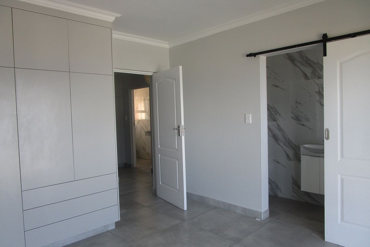 A modern, neutral bedroom featuring extensive built-in cupboards, large format floor tiles, and a sliding barn door leading to an en-suite bathroom.