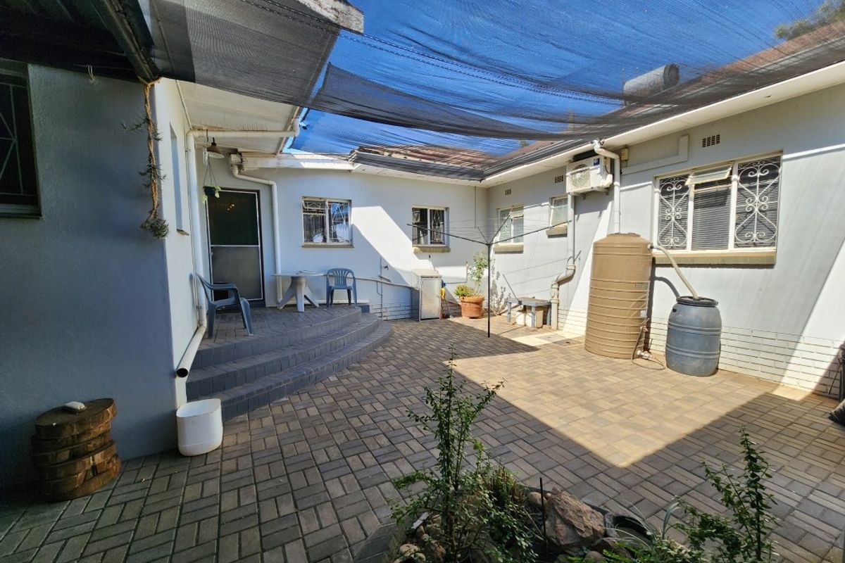 A paved rear courtyard area featuring a shade cloth canopy, water storage tanks, and direct access to the main dwelling.
