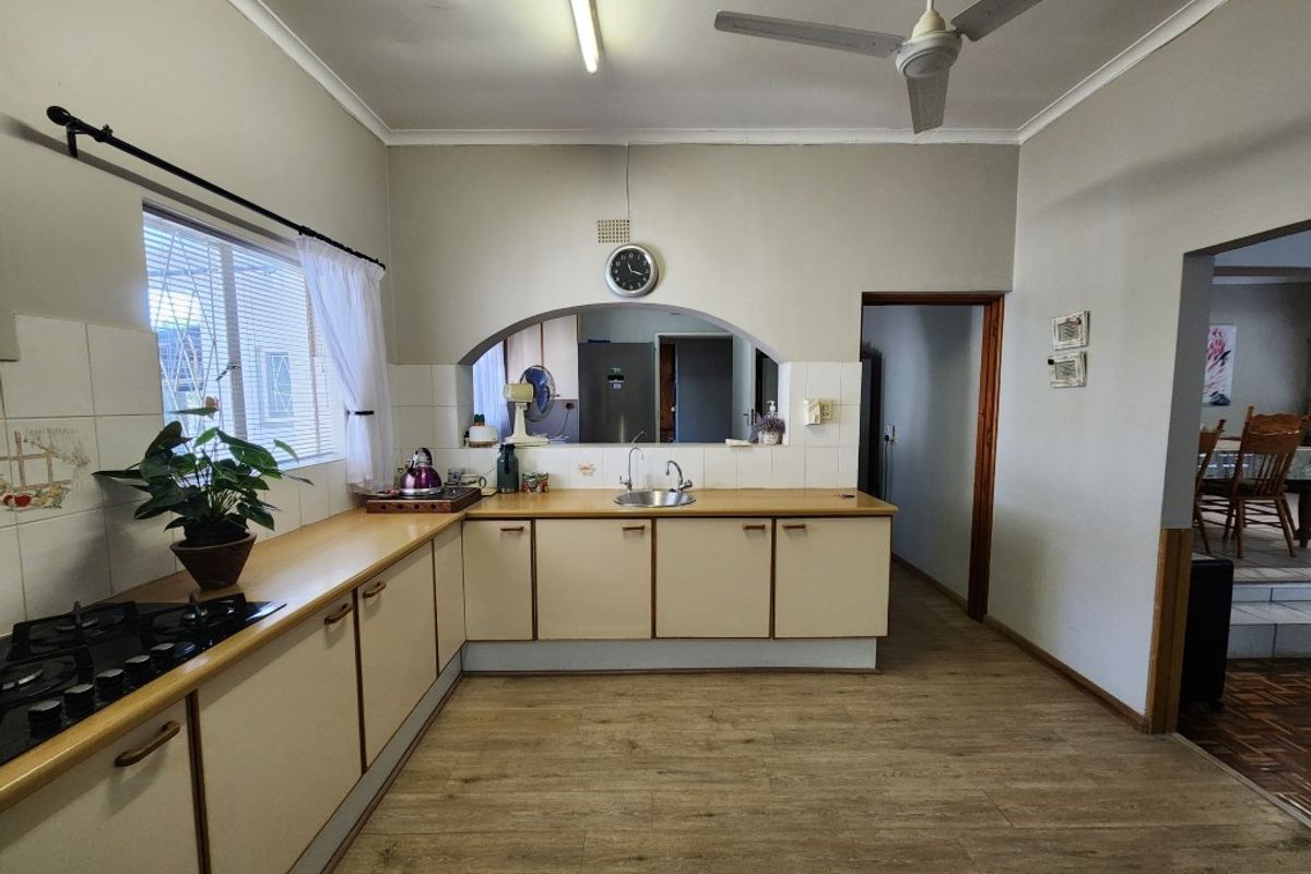A functional kitchen featuring laminate countertops, built-in cabinetry, a gas hob, and a serving hatch opening into the adjacent dining area.