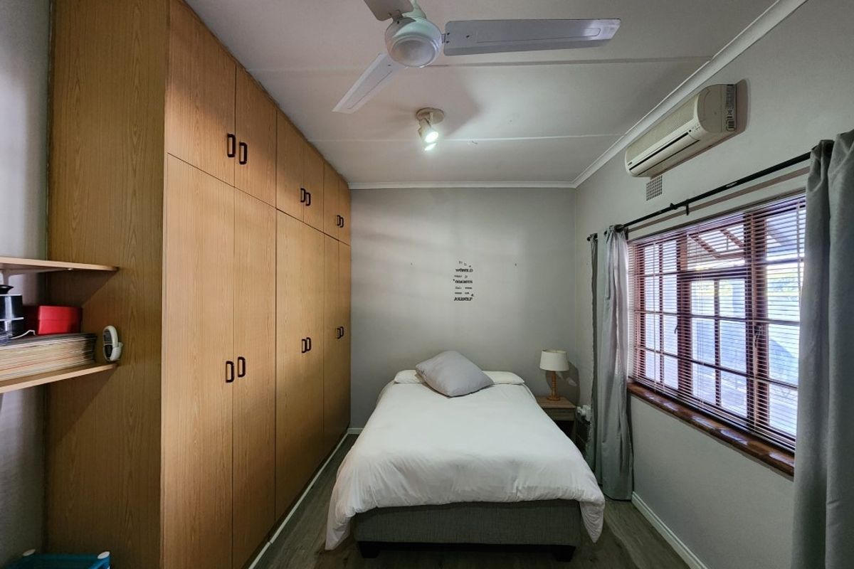 A bedroom featuring extensive built-in wooden cabinetry, a ceiling fan, and a wall-mounted air conditioning unit.