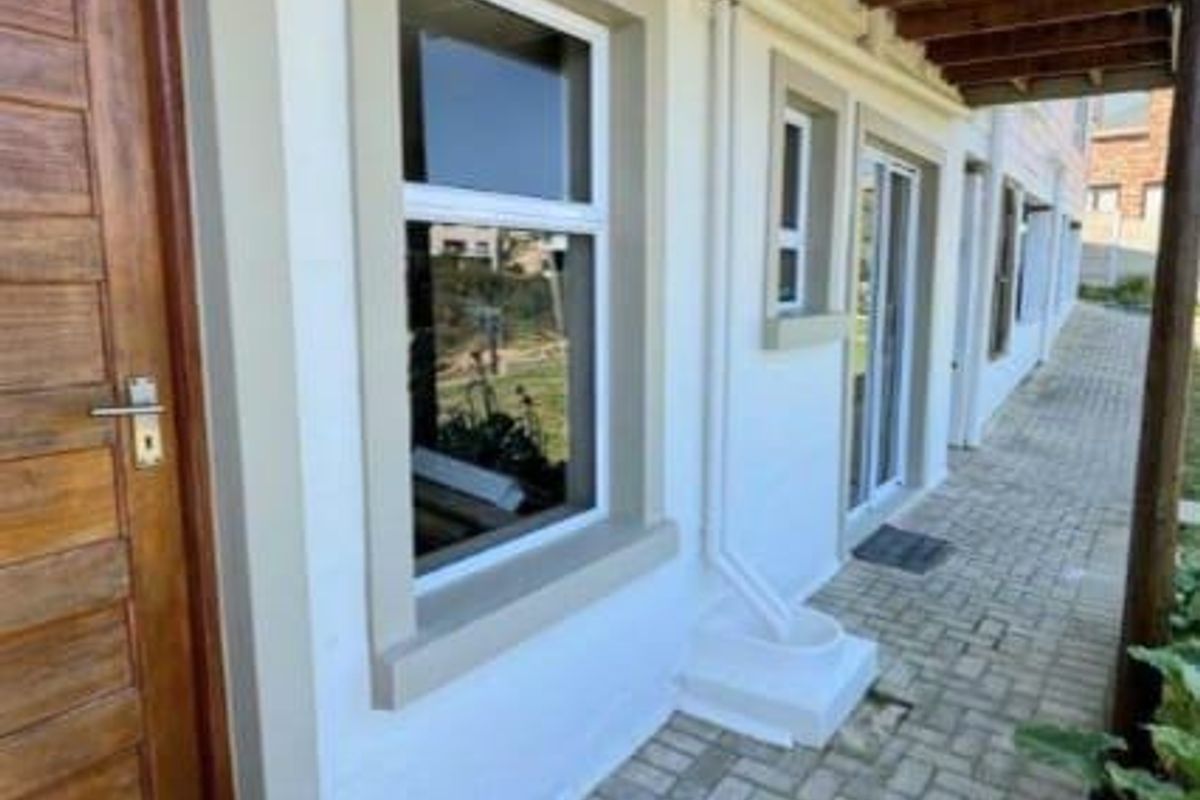 A paved exterior walkway along the side of the house featuring a wooden door, white exterior walls, and a timber-slatted pergola overhead.