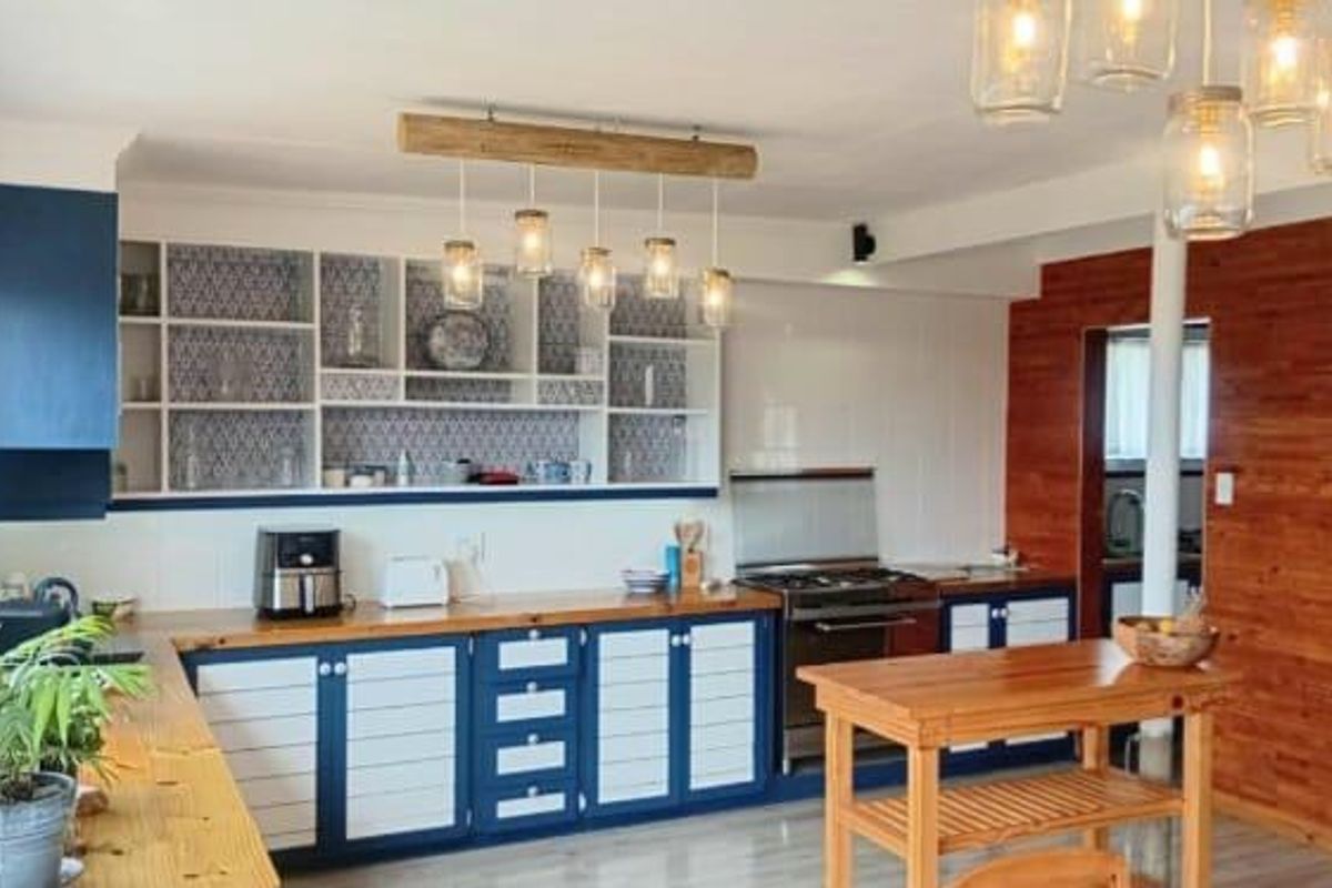 A well-maintained kitchen featuring blue and white cabinetry, wooden countertops, a gas stove, and decorative open shelving with patterned backing.