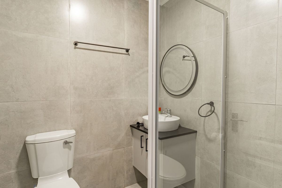 Modern bathroom featuring large format grey wall tiles, a floating vanity with a vessel sink, and a glass-enclosed shower.
